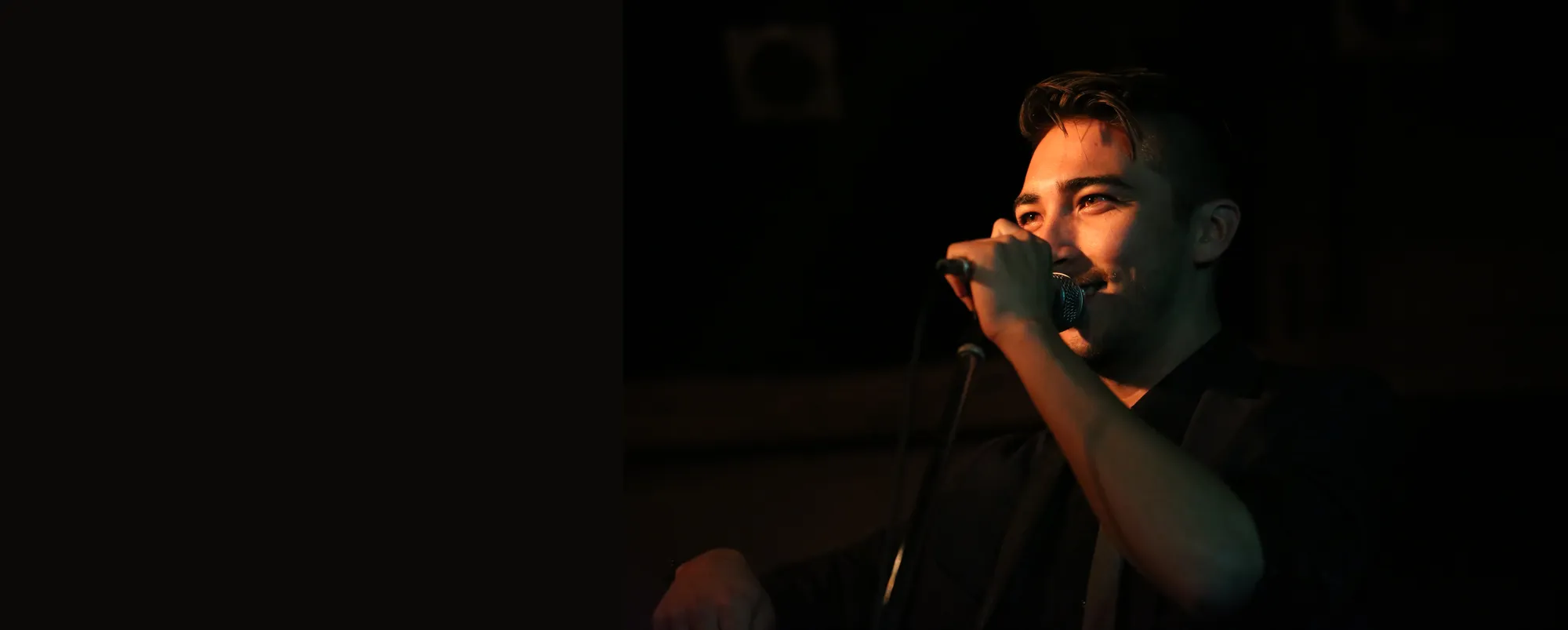 Alex Nishi singing into the mic under warm stage light
