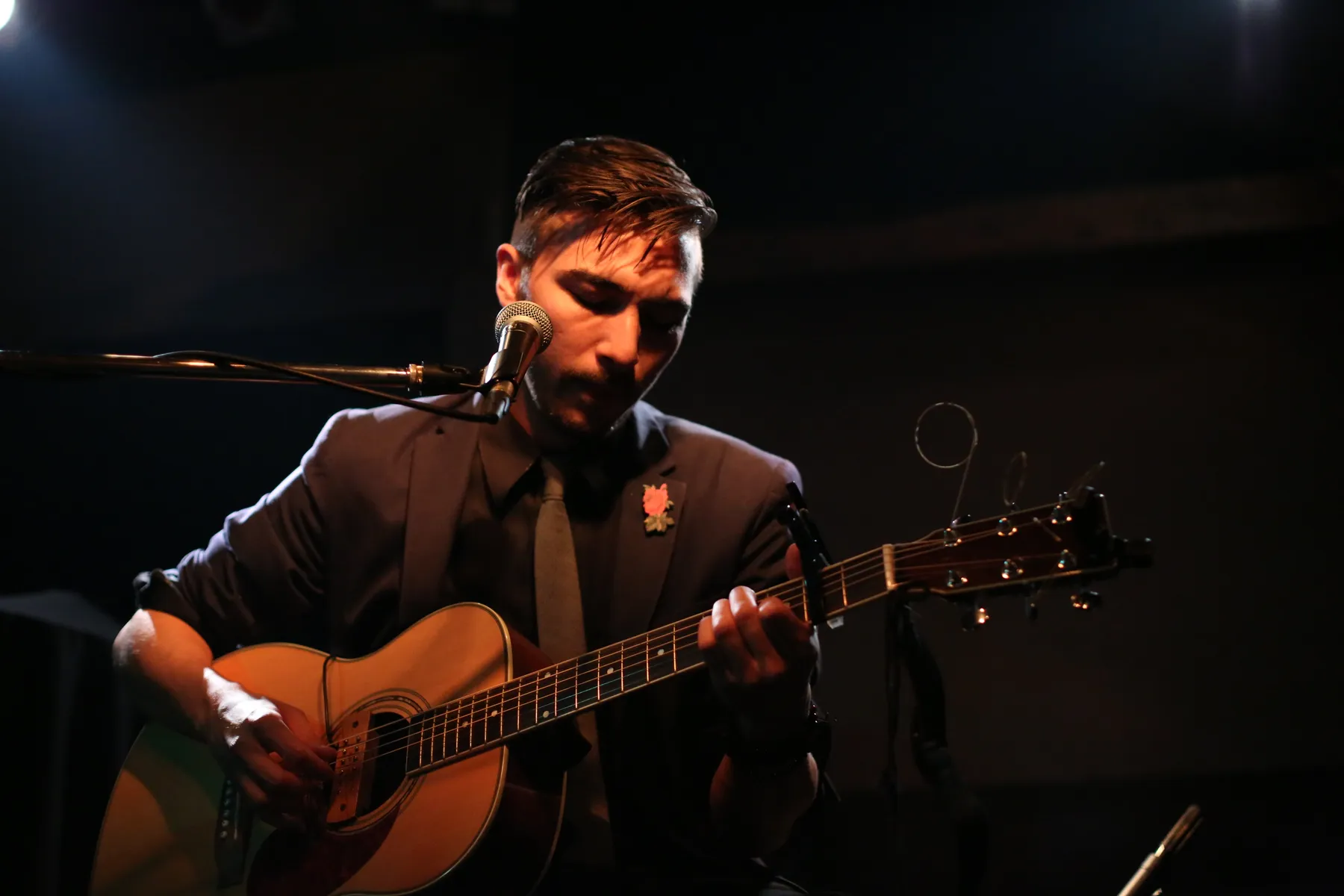 Alex Nishi singing and playing acoustic guitar at the mic